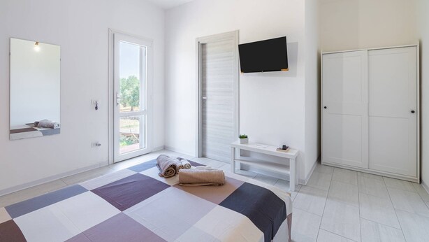 A bedroom with a bed, a TV mounted on the wall, a wardrobe, and a window with a view. - Villa Latina with Private Veranda, Wi-Fi, and Air Conditioning (Solarino)