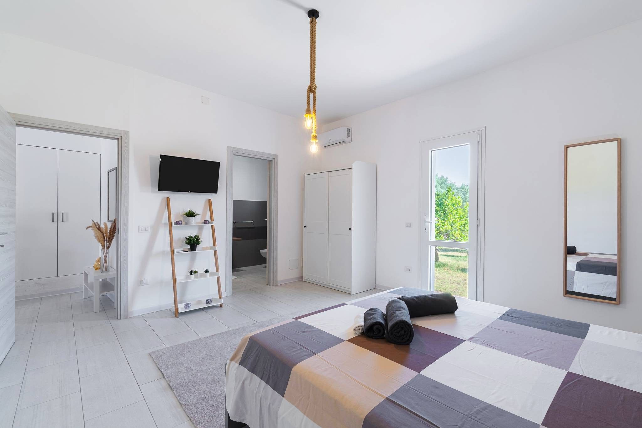 A modern bedroom with a large bed, a TV, a wardrobe, and a bathroom visible through an open door.
