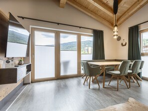 Ein moderner Essbereich mit Holztisch und -stühlen, großen Schiebeglasfenstern und Blick auf ein Gewässer.