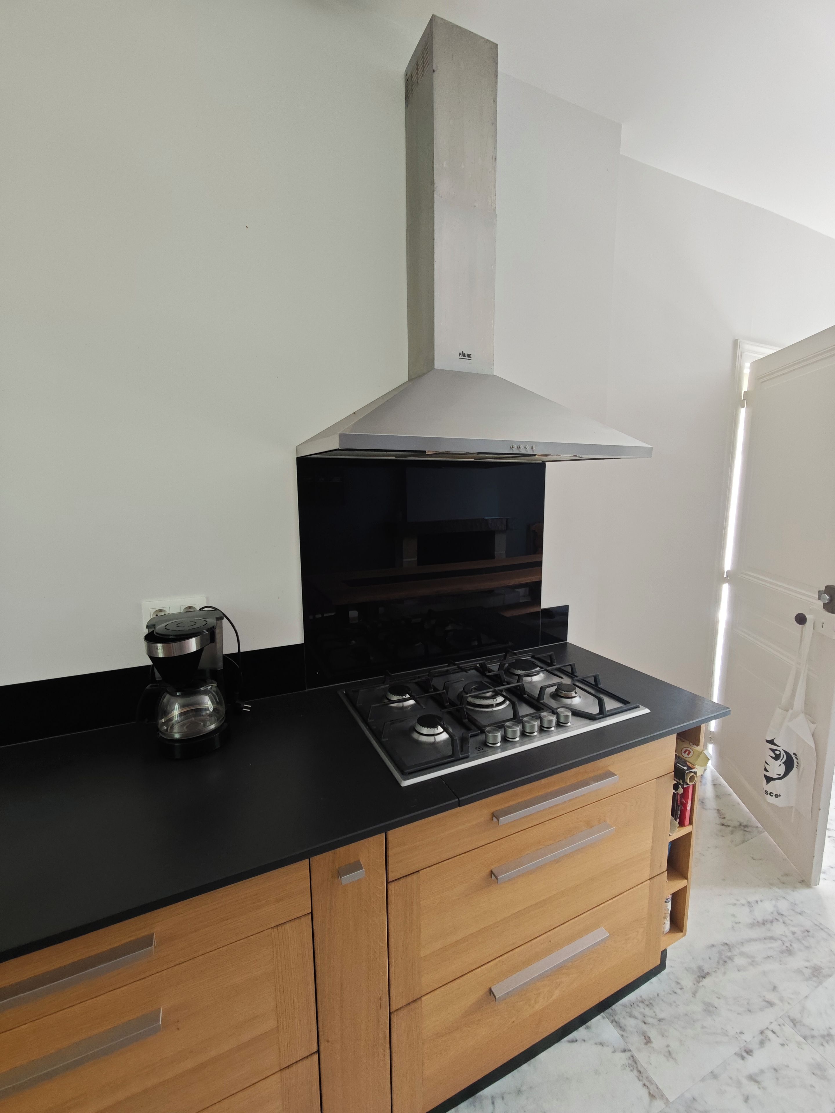 A kitchen with a gas stove, a coffee maker, wooden cabinets, and a white wall.