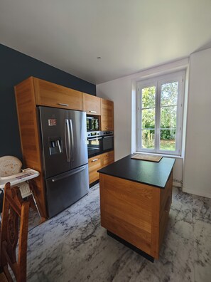 A kitchen with a refrigerator, oven, and wooden cabinets. - Meurdrac's Rest (La Meurdraquière)