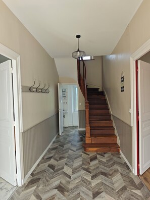 A hallway with a herringbone-patterned floor, a wooden staircase, and a ceiling light fixture. - Meurdrac's Rest (La Meurdraquière)