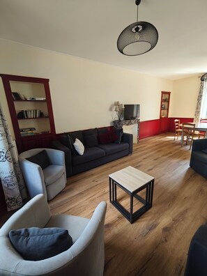A living room with a sofa, armchairs, a coffee table, a bookshelf, and a television. - Meurdrac's Rest (La Meurdraquière)