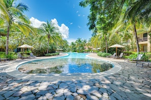 A pool with a curved edge, surrounded by lounge chairs and palm trees. - Pacifico Townhome w/ 4 Resort Pools & Beach Club! (Sardinal)