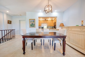 A dining area with a glass-top table, wooden chairs, a kitchen in the background, and a staircase on the left. - Pacifico Townhome w/ 4 Resort Pools & Beach Club! (Sardinal)