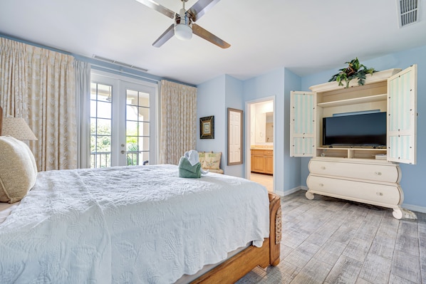 A bedroom with a bed, a ceiling fan, a television, and a bathroom visible through an open door. - Pacifico Townhome w/ 4 Resort Pools & Beach Club! (Sardinal)