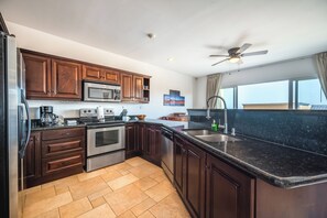 Une cuisine moderne avec des meubles en bois foncé, des appareils en acier inoxydable, un plan de travail en granit noir et une grande fenêtre offrant une belle vue.