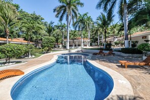 Une piscine dont le bord est recouvert de carrelage, entourée de palmiers et de chaises longues.