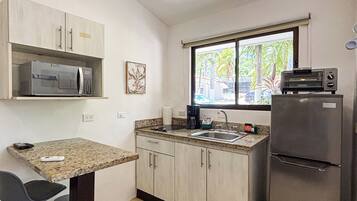 Una cocina compacta con microondas, cafetera, refrigerador y ventana con vista a palmeras.