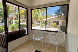 A room with two white chairs, a large window with a view of palm trees and buildings, and a tiled floor. - Walk to Beach! Studio w/ Pool Access at Club Voca (Sardinal)