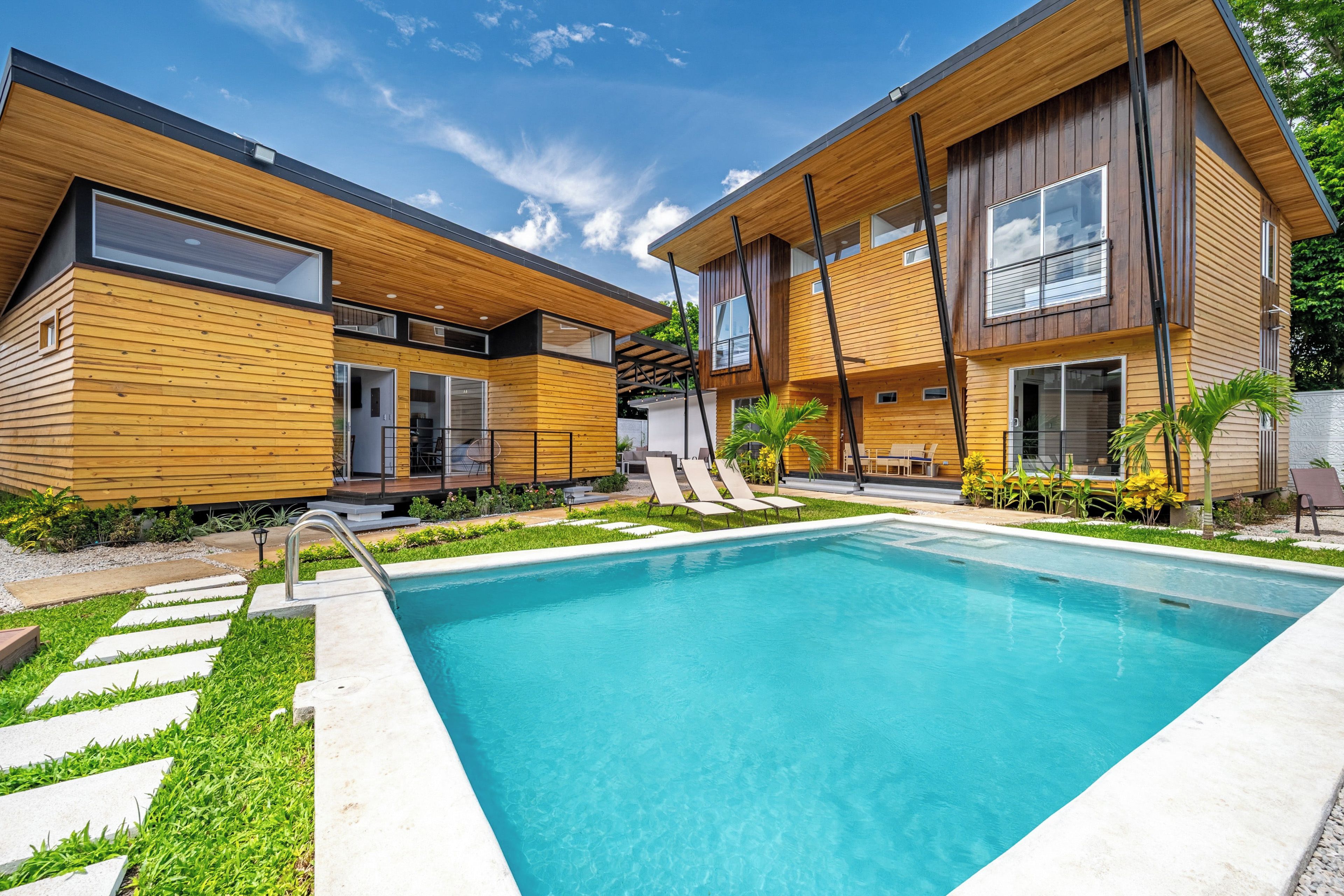 Una casa moderna de dos pisos con piscina, fachada de madera y un patio cubierto.