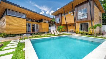 Una casa moderna de dos pisos con piscina, fachada de madera y un patio cubierto.