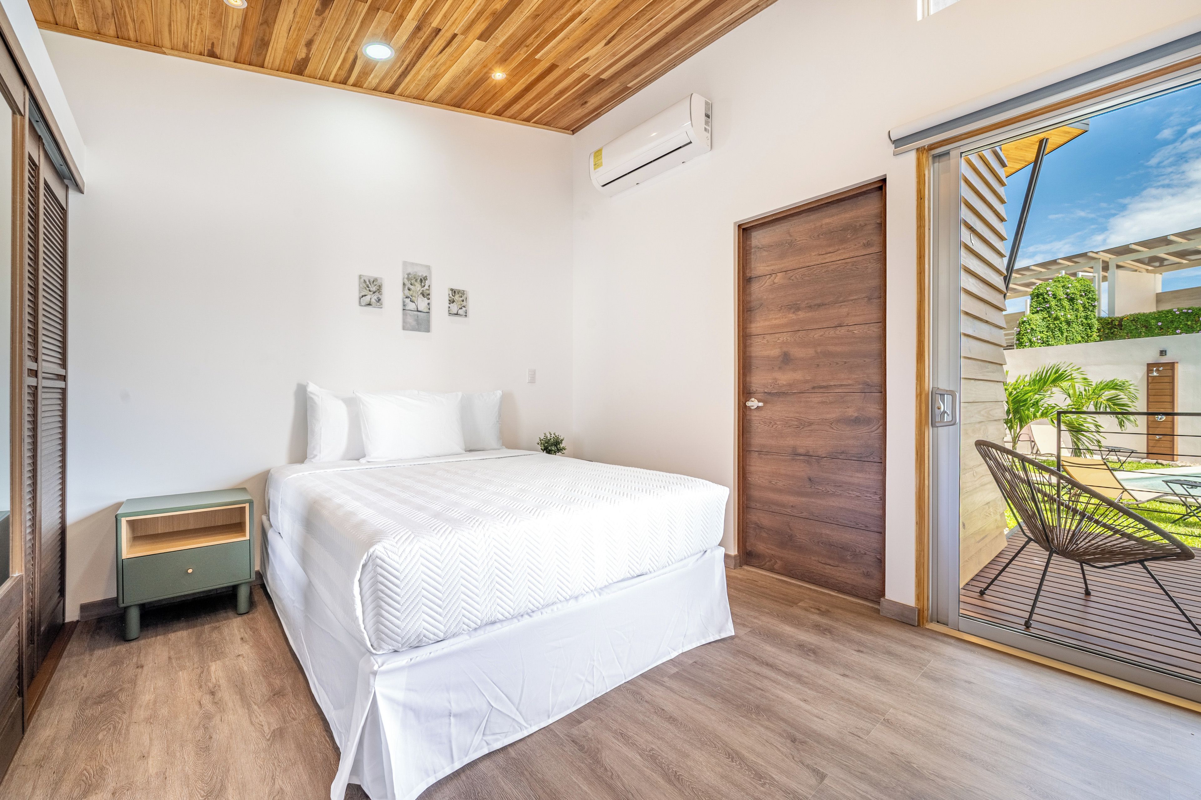 A bedroom with a bed, a nightstand, a wooden ceiling, and a sliding glass door leading to an outdoor area.