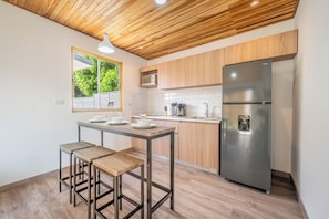 A modern kitchen with a wooden ceiling, a stainless steel refrigerator, and a dining area with stools.
