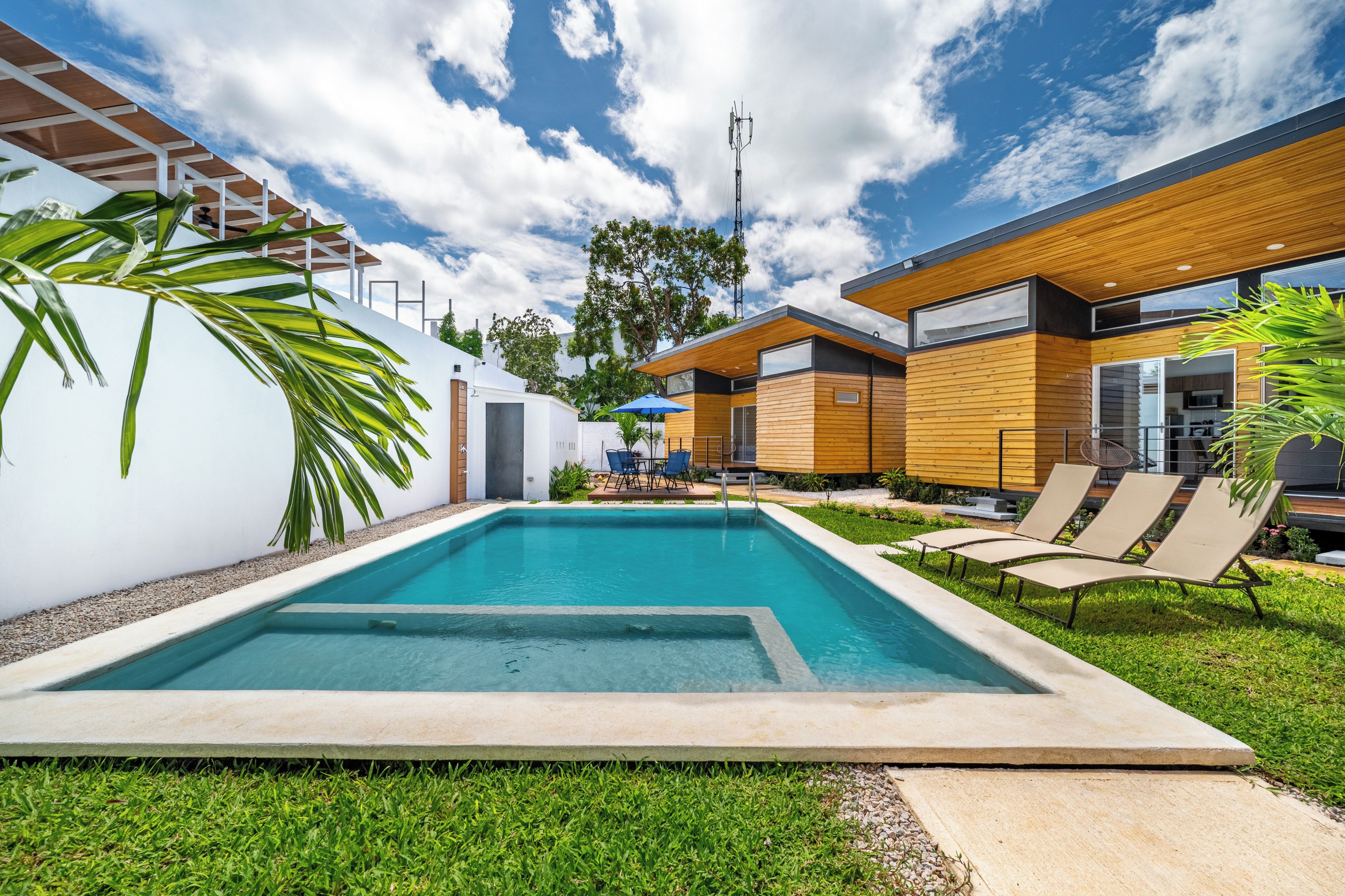 Un área de piscina moderna con piscina rectangular, sillas de descanso y terraza de madera.