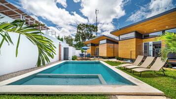 Un área de piscina moderna con piscina rectangular, sillas de descanso y terraza de madera.
