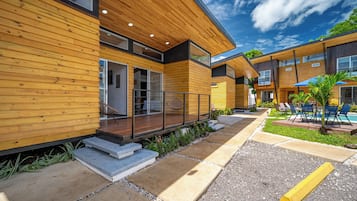 A modern building with wooden exterior walls, large windows, and a covered outdoor seating area with chairs and a pool.