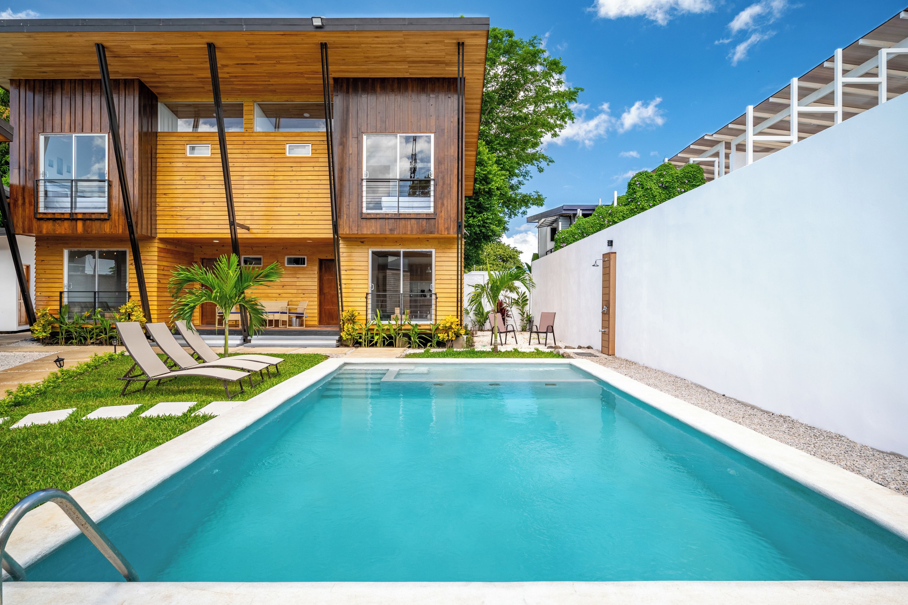 Un moderno edificio de dos pisos con piscina, mobiliario exterior y un jardín bien cuidado.
