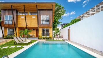 Un moderno edificio de dos pisos con piscina, mobiliario exterior y un jardín bien cuidado.