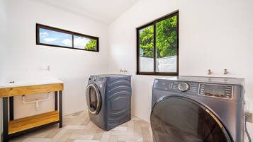 A laundry room with two washing machines, a sink, and a window with a view of greenery.
