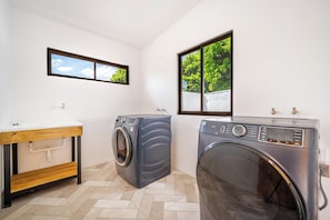 A laundry room with two washing machines, a sink, and a window with a view of greenery. - Luxurious 6-unit Oasis < 1 Mi to Playas Del Coco! (Sardinal)