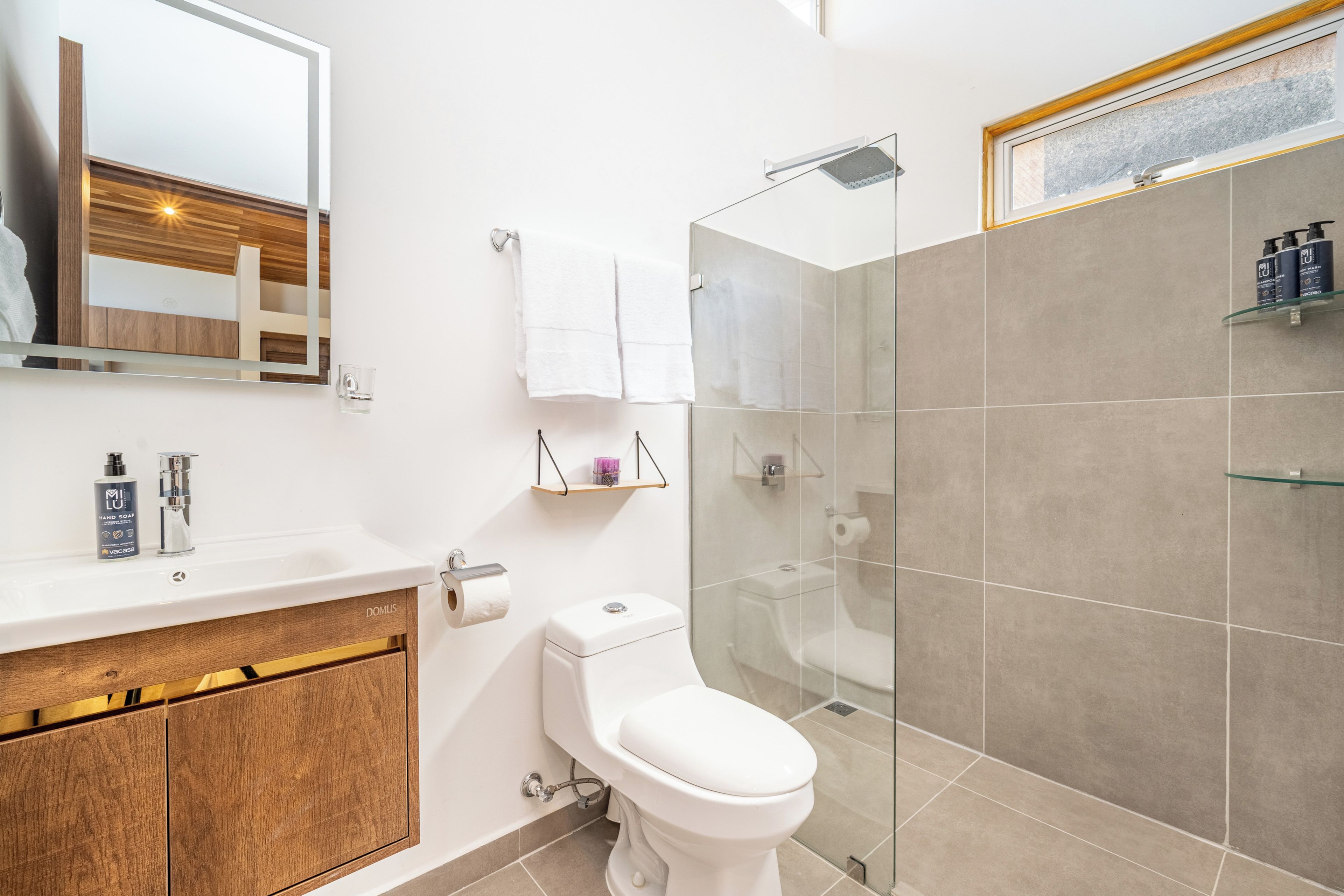 A modern bathroom with a white sink, a toilet, a glass shower enclosure, and a mirror.