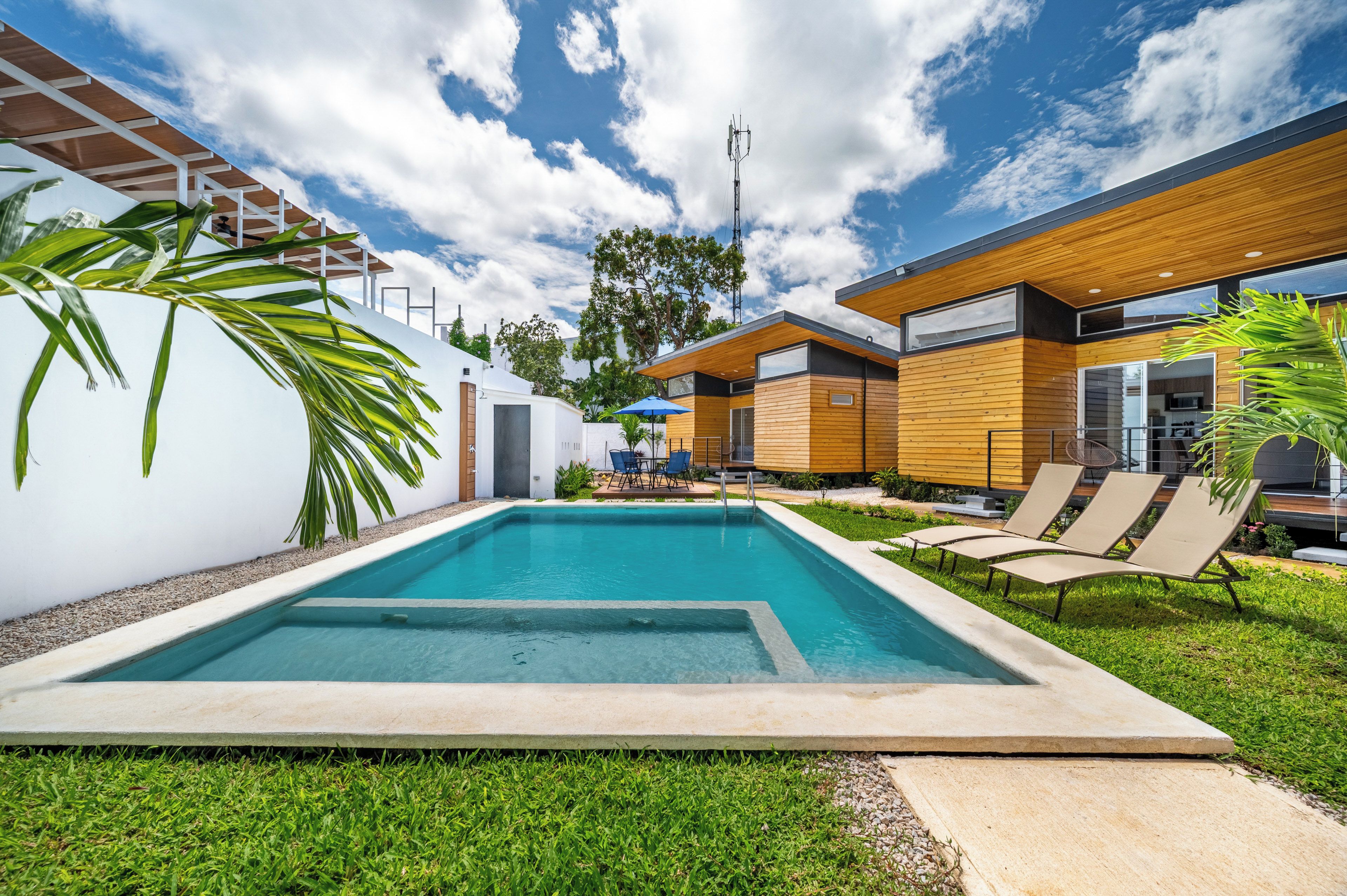 A modern outdoor pool area with a wooden deck, lounge chairs, and a clear blue sky.