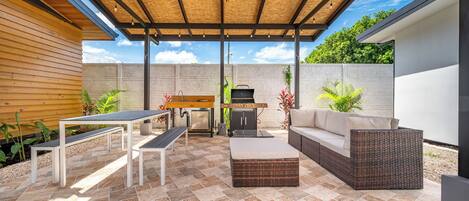 A covered patio with a ceiling fan, outdoor furniture, a barbecue grill, and a stone wall.