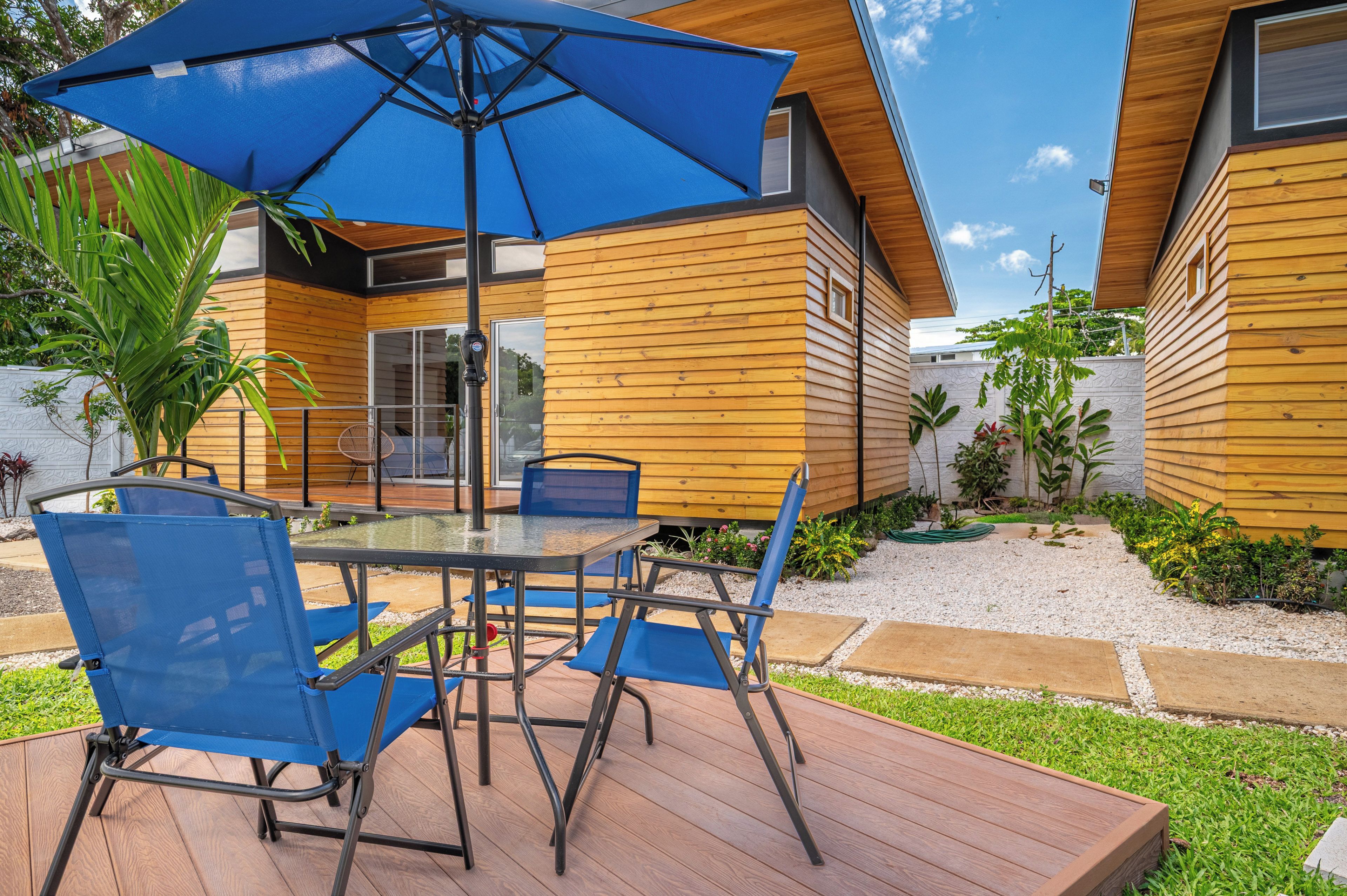 A deck with a table and chairs, an umbrella, and a wooden house with a window.