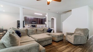 A modern living room with a sectional sofa, a single chair, and a kitchen in the background.