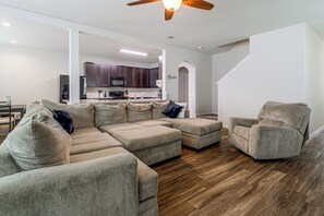 A modern living room with a sectional sofa, a single chair, and a kitchen in the background.
