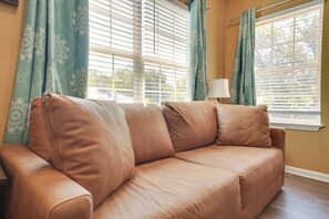 A tan leather sofa with a white cushion, positioned in front of a window with blinds, and a lamp on a side table. - 2 Mi to Downtown! Central San Antonio Rental (San Antonio)
