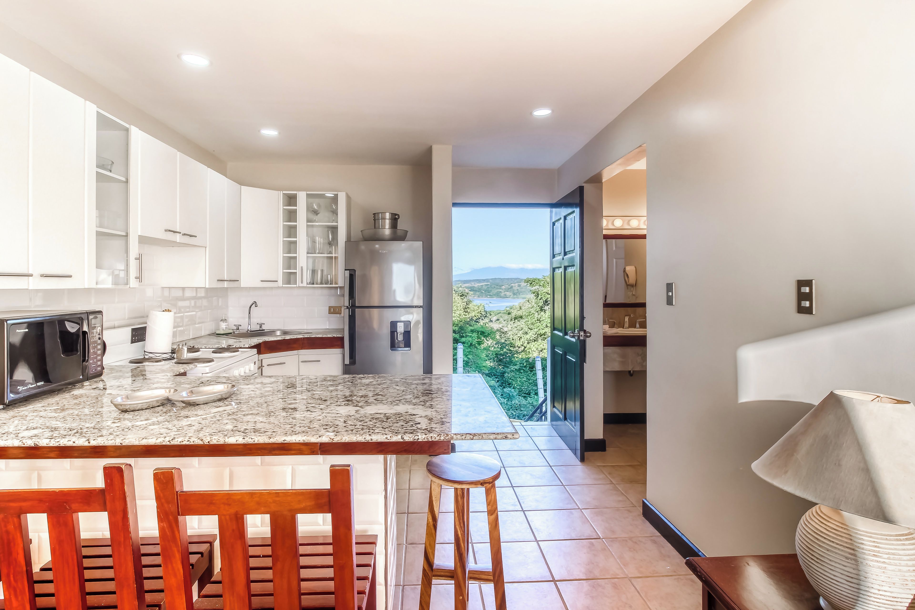 A modern kitchen with white cabinetry, a granite countertop, and a view of the outdoors.