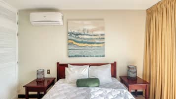Quarto de hotel com cama, ar-condicionado na parede, um quadro e cortina.