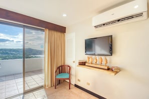 A room with a television mounted on the wall, a chair, a wooden shelf with figurines, and a sliding glass door leading to a balcony with a view of the landscape. - Playa Hermosa Resort Villa w/ Ocean Views & Pool! (Sardinal)