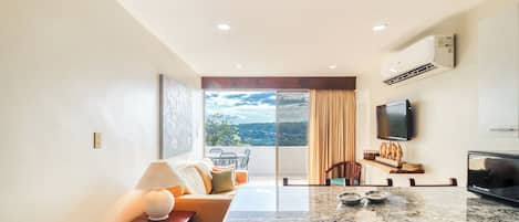 A modern kitchen with a large island, a dining area with a table and chairs, a sofa, and a TV mounted on the wall.