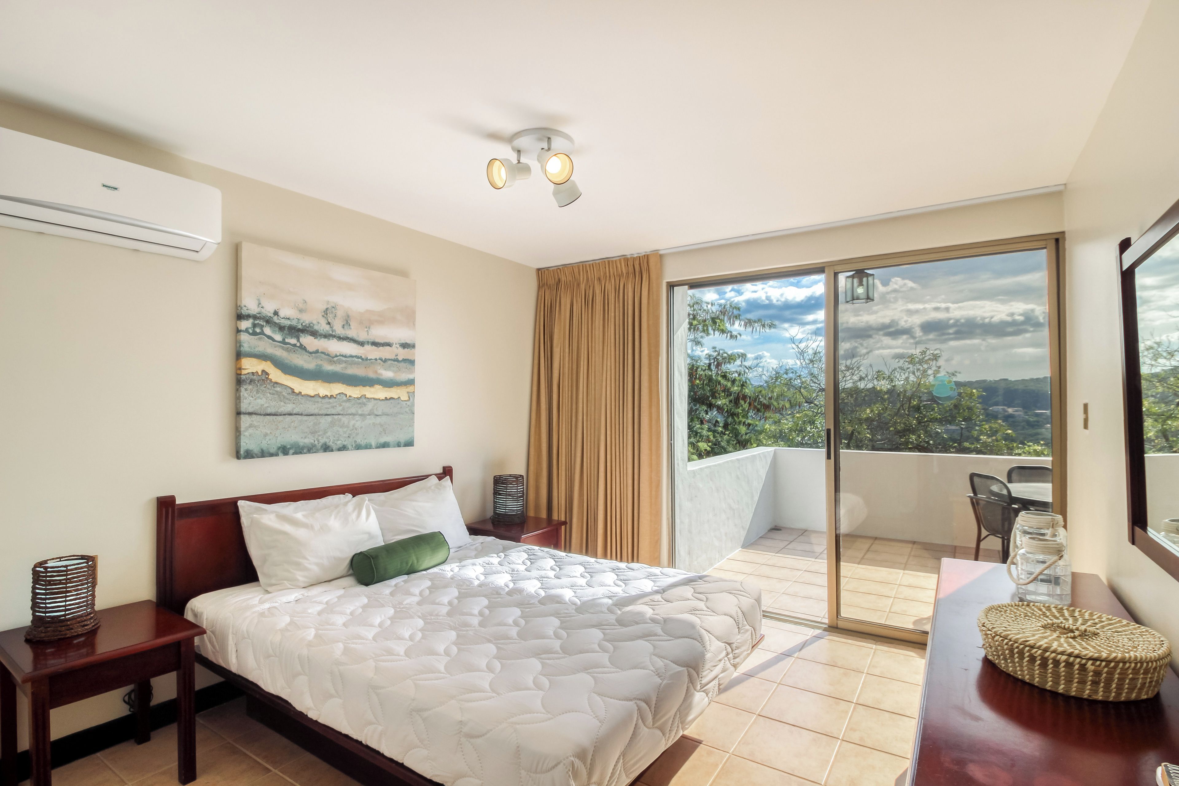 A hotel room with a bed, a painting, a view of the outdoors, and a balcony.