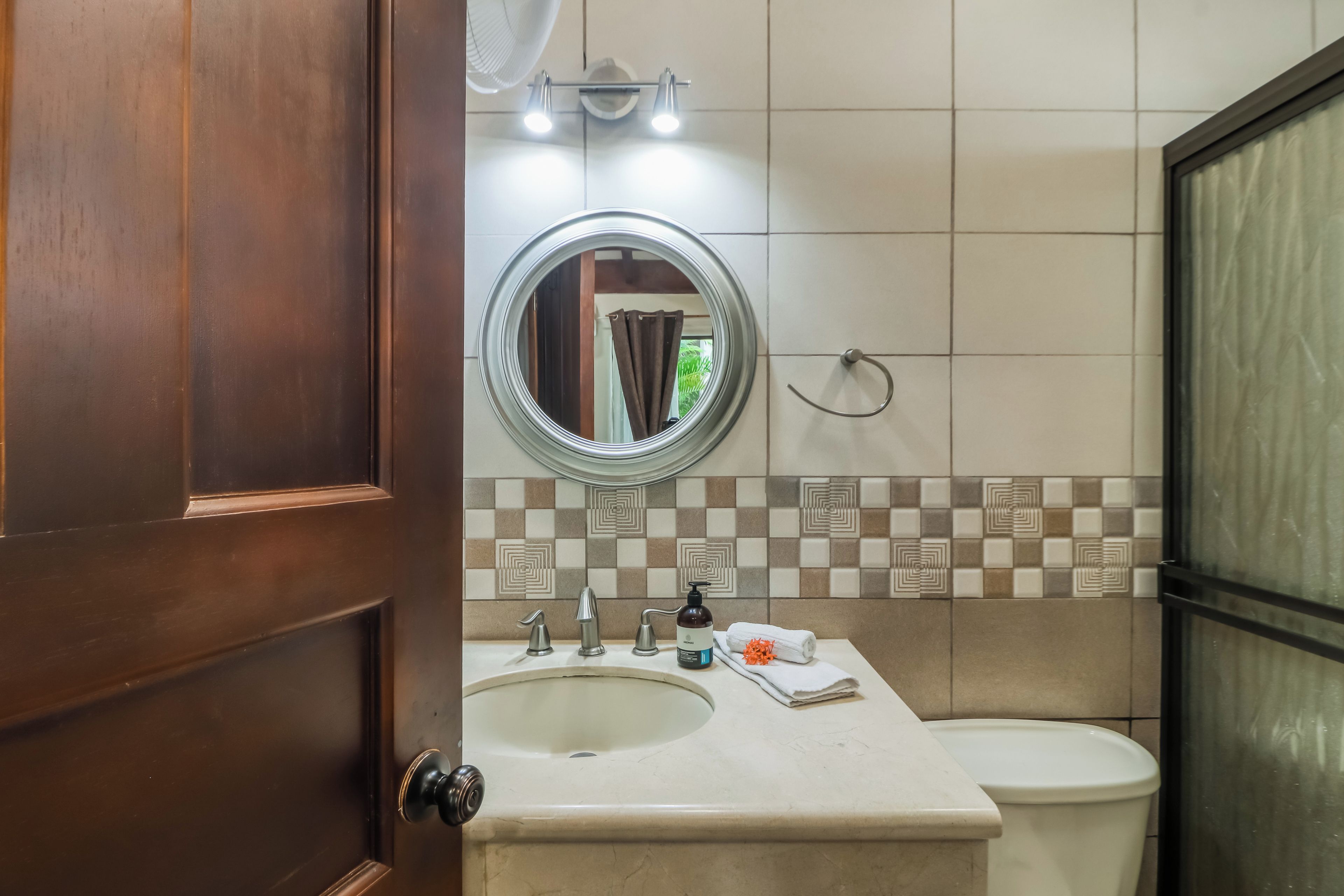 Un baño con puerta de madera, un espejo redondo, un lavabo, un inodoro y una toalla sobre el mostrador.