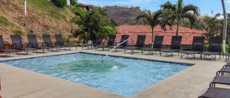 A swimming pool with lounge chairs and a building with a tiled roof in the background.