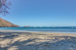 Uma praia com céu claro, águas calmas e barcos.