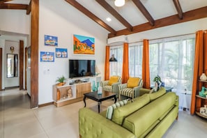 A living room with a green sofa, striped armchairs, a flat-screen TV, and artwork on the wall. - Pool & Beach Access: 2-unit Base in Playa Hermana (Sardinal)