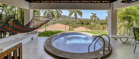 A pool area with a hot tub, a hammock, and a view of a mountainous landscape.