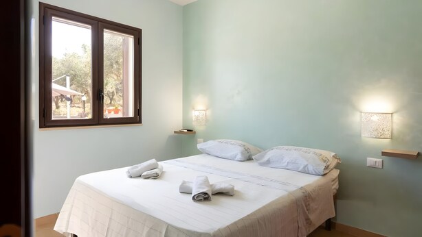 A bedroom with a bed, two bedside lamps, a window, and a view of the outdoors. - Villa Rosa with Private Pool, Wi-Fi, and Air Conditioning (Partinico)