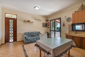 A compact living space with a sofa, a table, a kitchen area with a TV, and a door leading outside.