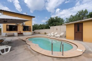 Ein Poolbereich mit Wohnbereich, ausgestattet mit einem gebogenen Pool, Liegestühlen, einer Bank und einer Tür.