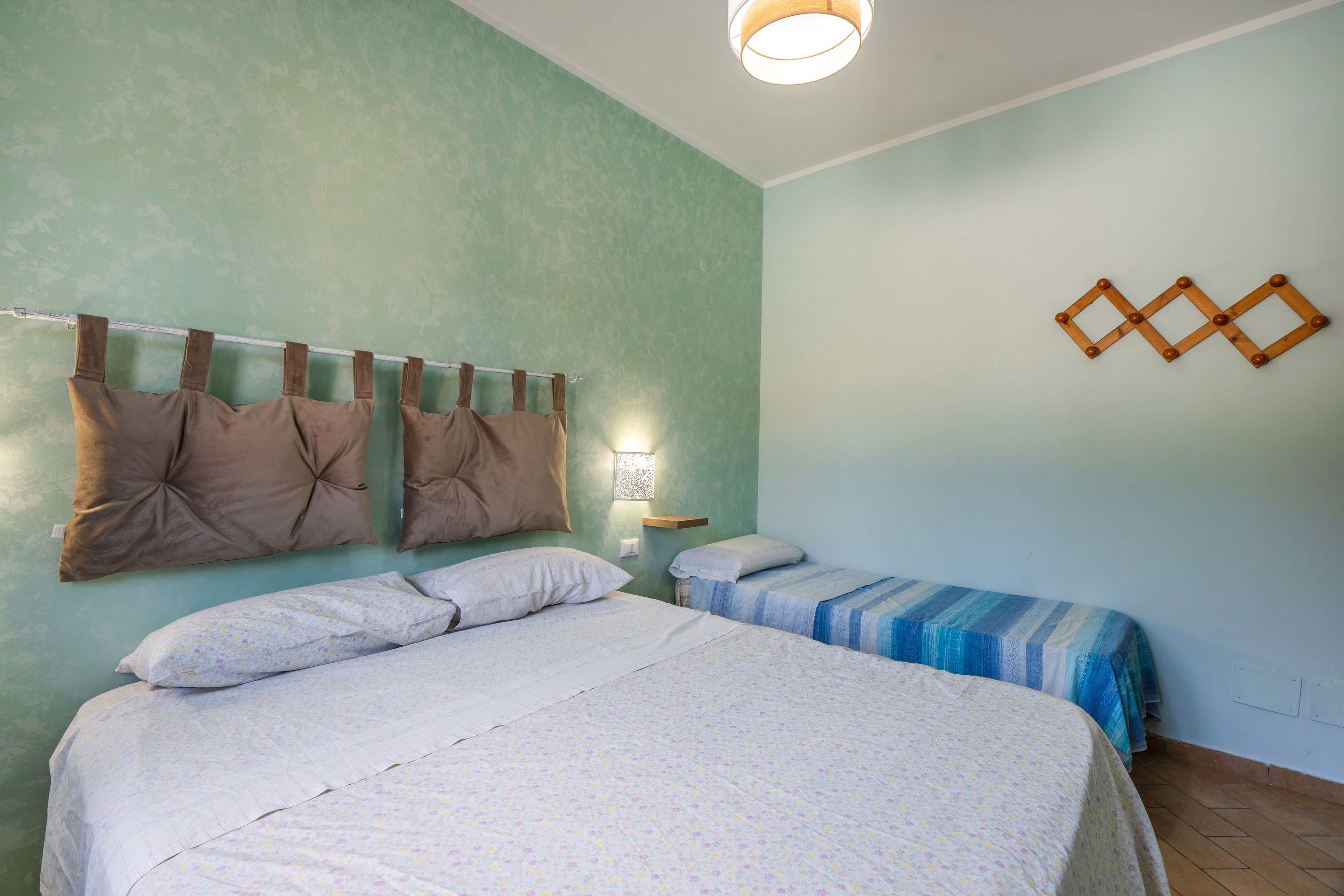 A bedroom with two beds, a hanging light fixture, and a wall-mounted decorative item.