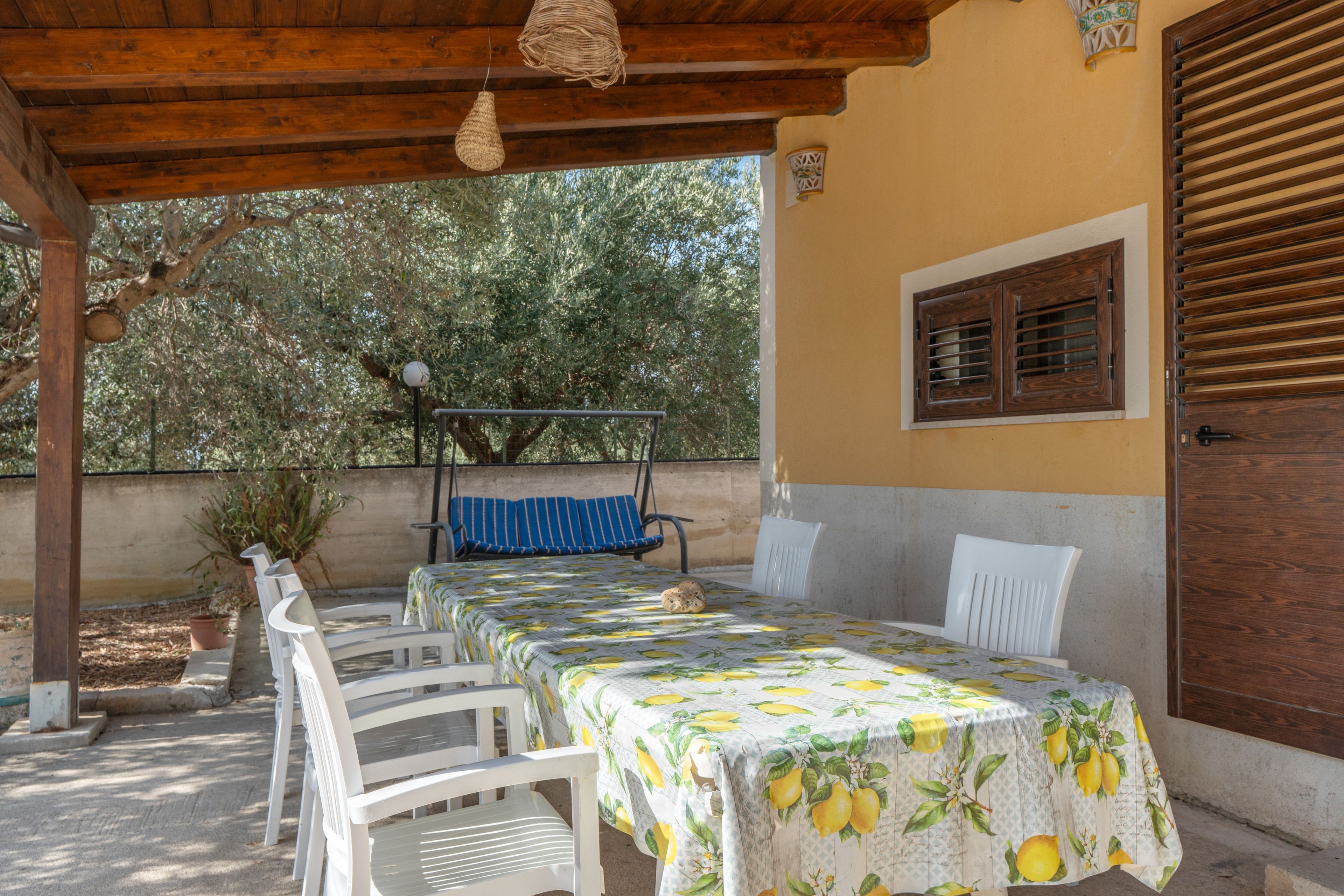 An outdoor patio with a table and chairs, a hanging light fixture, and a window with shutters.