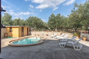 A swimming pool with lounge chairs, surrounded by trees and a small building.