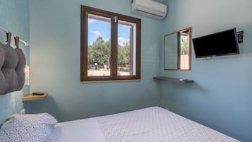 Una habitación con cama, ventana, aire acondicionado, televisor y un perchero para toallas.