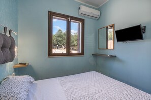 A room with a bed, a window, an air conditioner, a TV, and a towel rack.